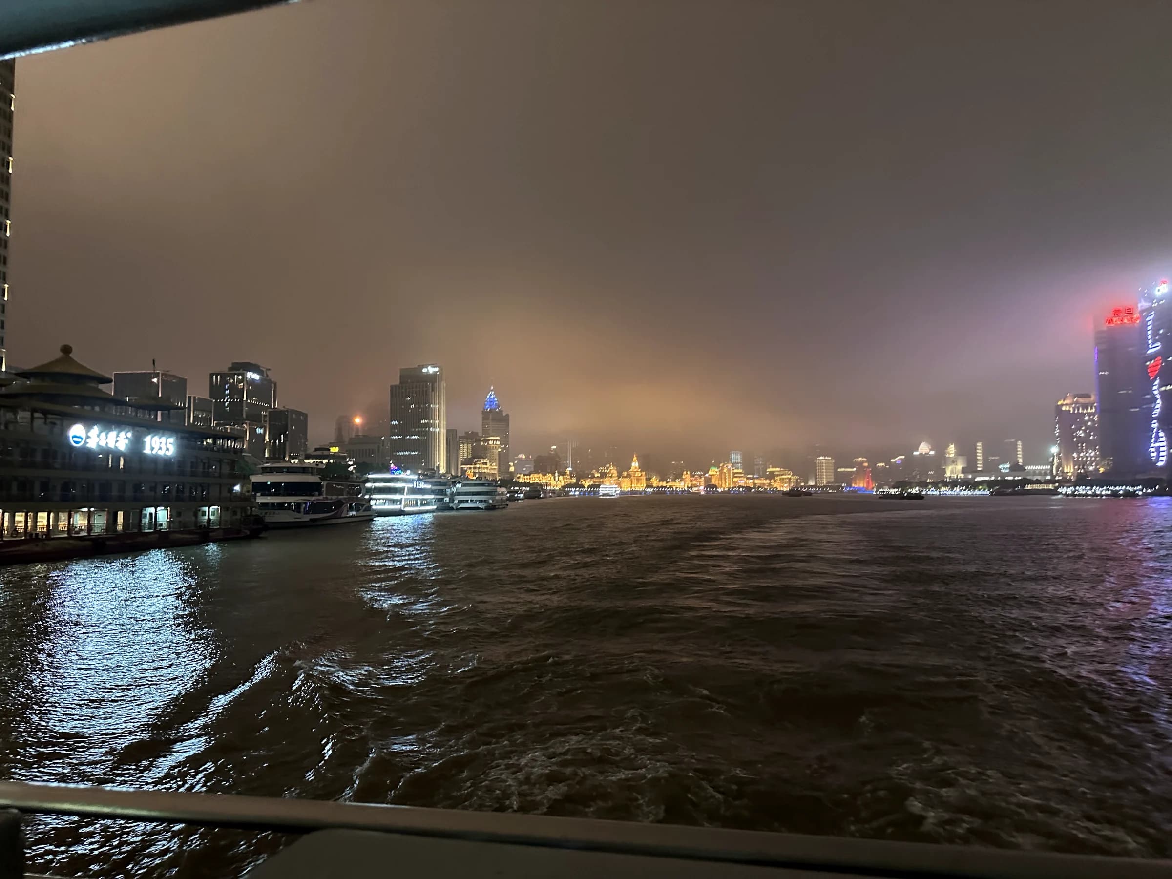 A ferry wake opening across the Huangpu River at night